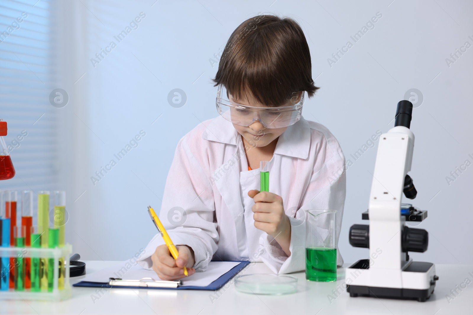 Photo of Little boy doing chemical experiment at desk indoors