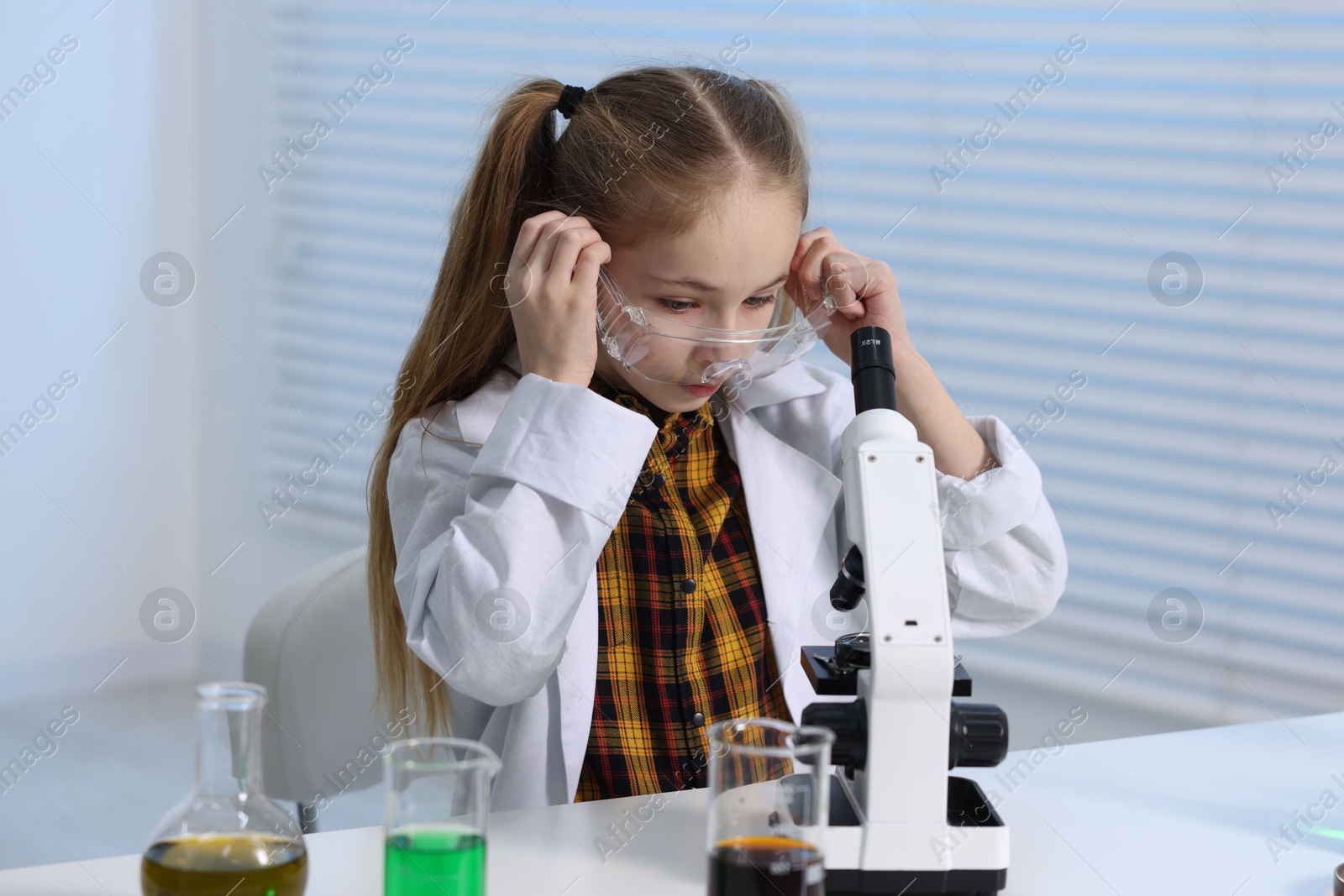 Photo of Little girl working with microscope at desk indoors