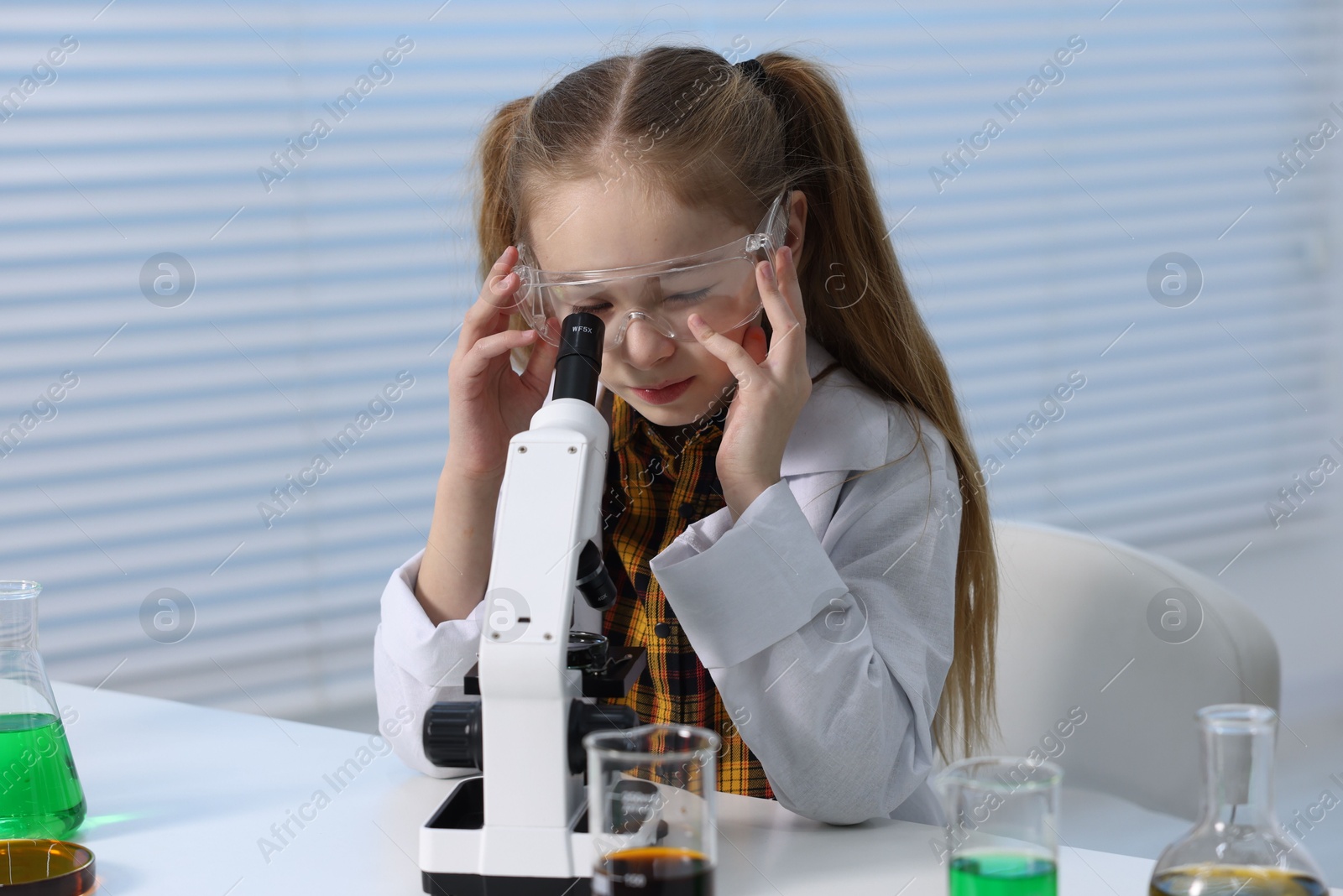 Photo of Little girl working with microscope at desk indoors