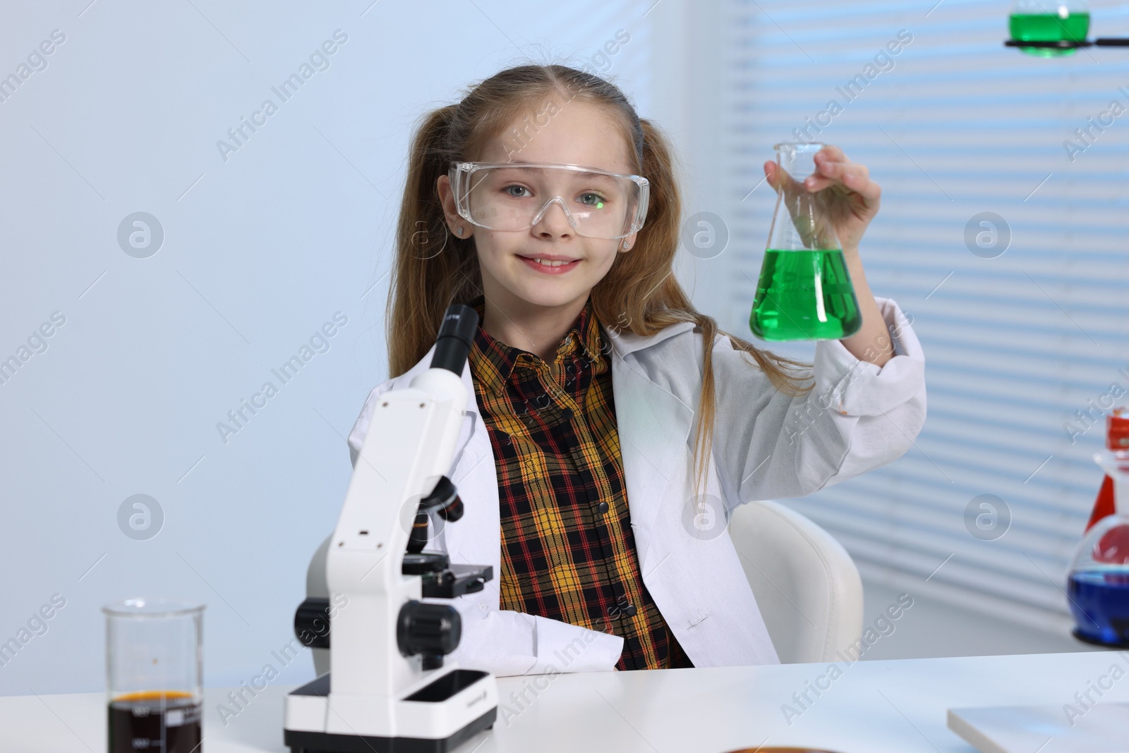 Photo of Little girl doing chemical experiment at desk indoors