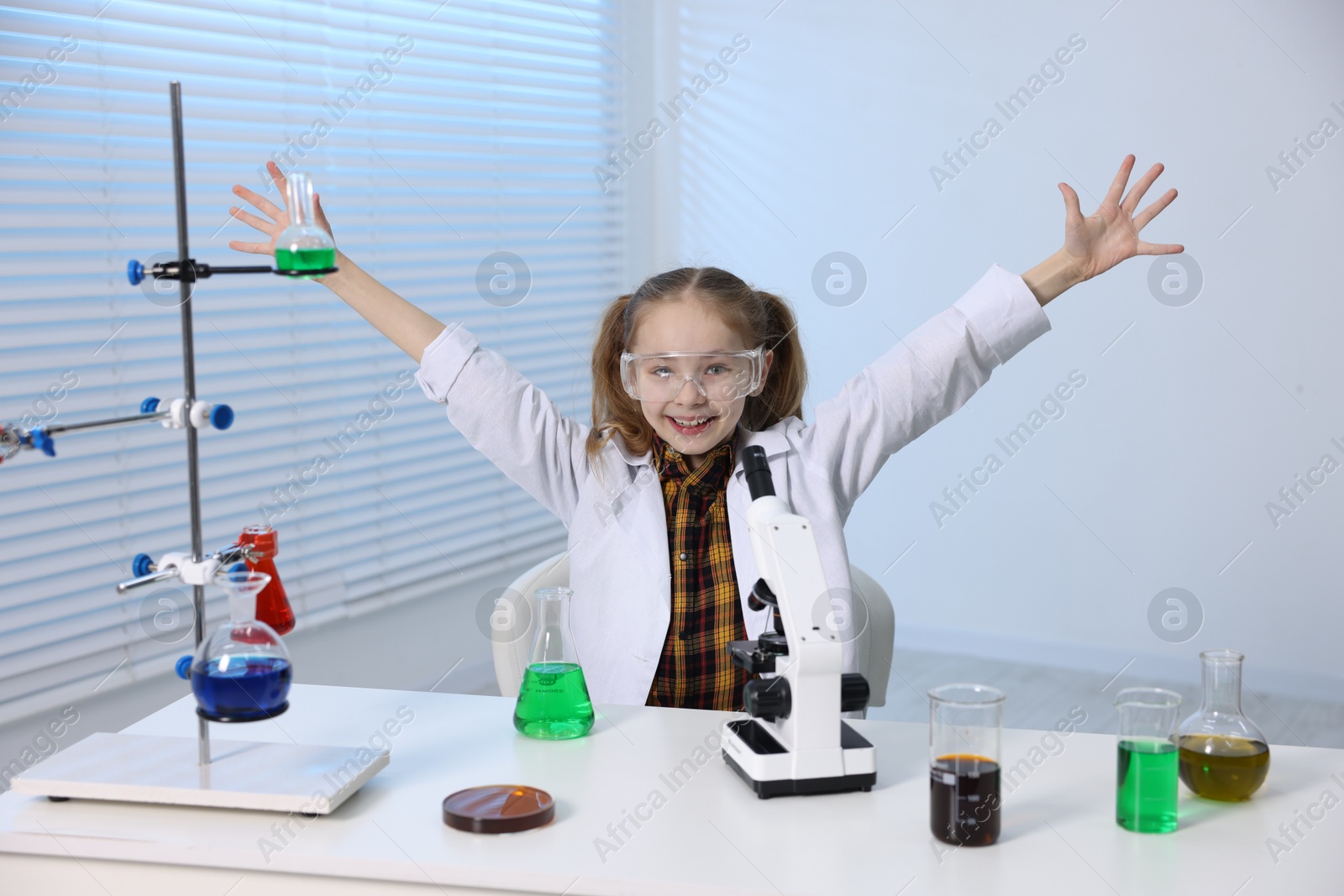 Photo of Little girl doing chemical experiment at desk indoors