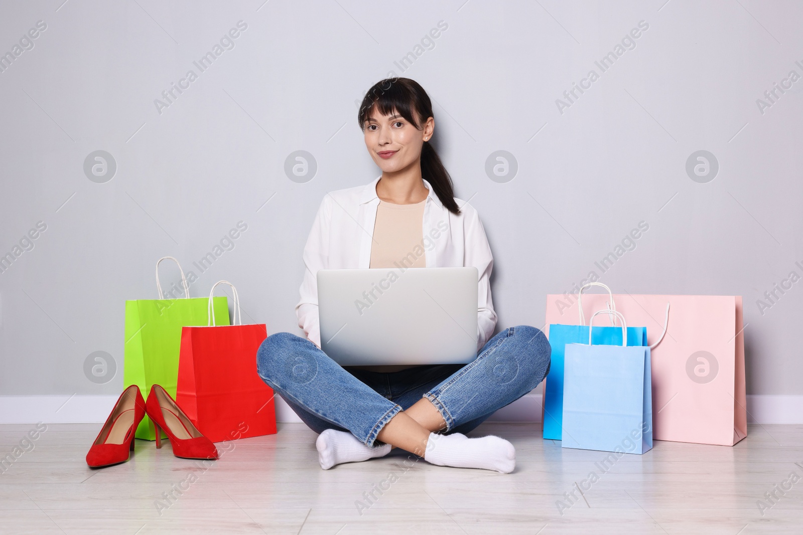 Photo of Internet shopping. Beautiful woman with laptop and colorful bags sitting near grey wall