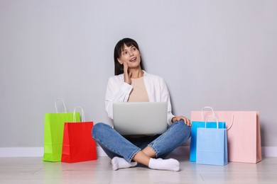 Photo of Internet shopping. Happy woman with laptop and colorful bags sitting near grey wall