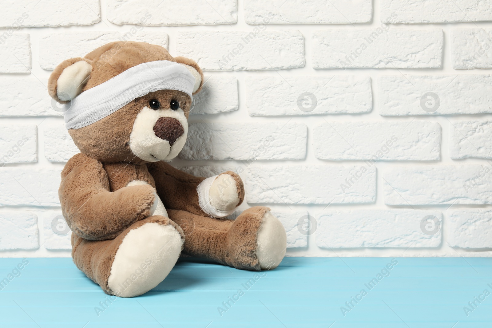 Photo of Teddy bear with bandages on light blue wooden table against white brick wall, space for text