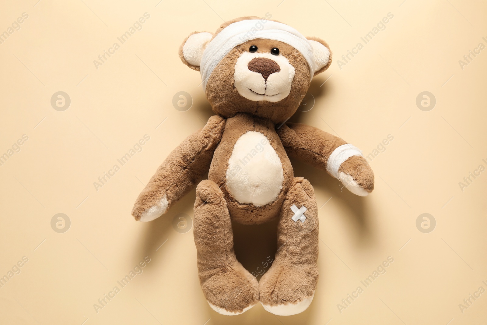 Photo of Teddy bear with bandages and sticking plasters on beige background, top view