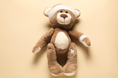 Photo of Teddy bear with bandages and sticking plasters on beige background, top view