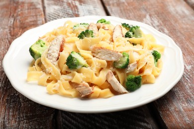 Photo of Delicious pasta Alfredo with chicken, cheese and broccoli on wooden table, closeup