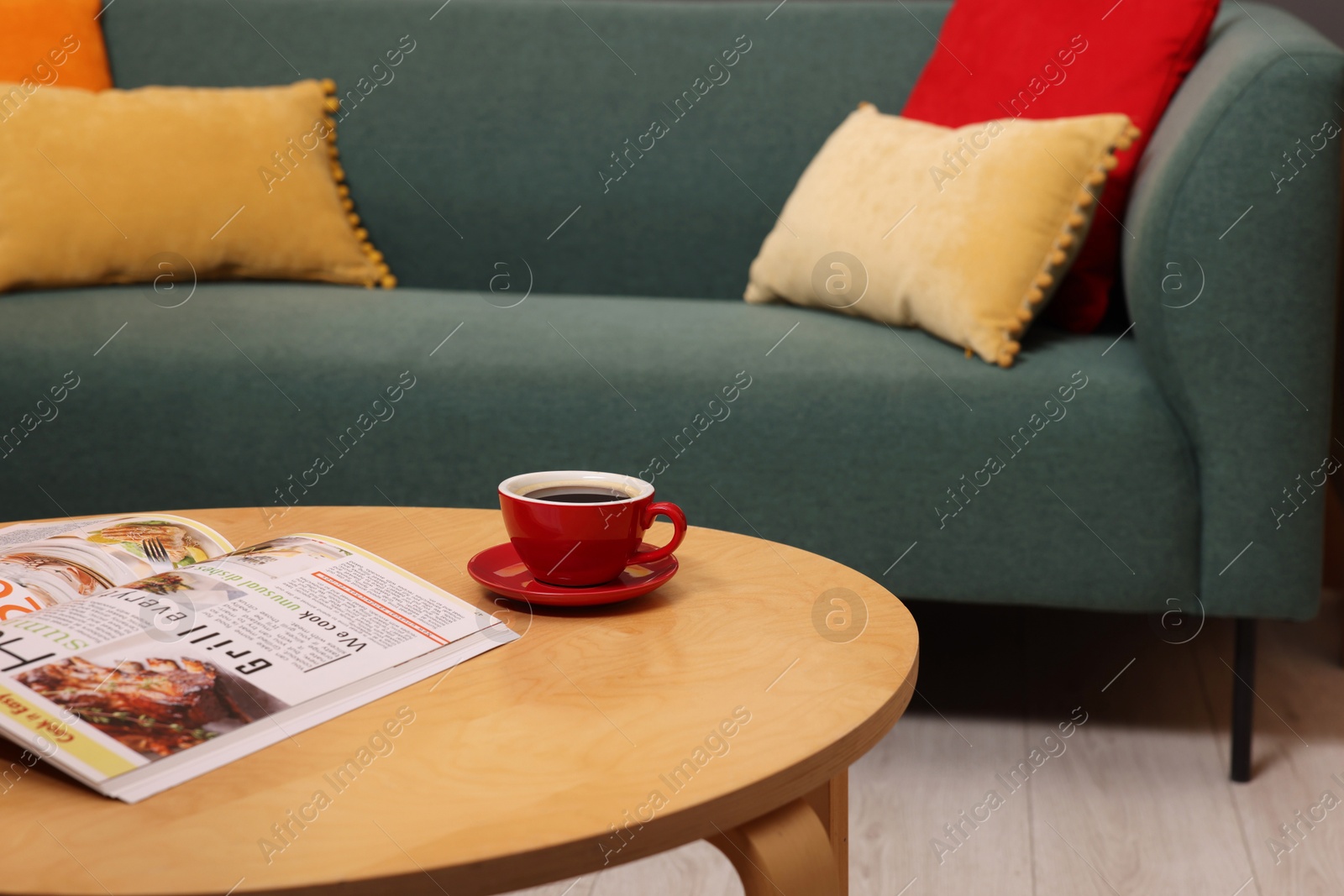 Photo of Wooden coffee table with cup of drink and magazine near sofa indoors, closeup