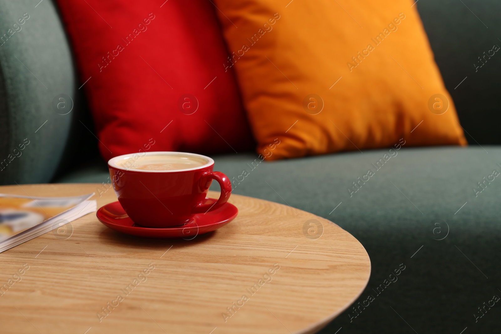 Photo of Wooden coffee table with cup of drink and magazine near sofa indoors, closeup