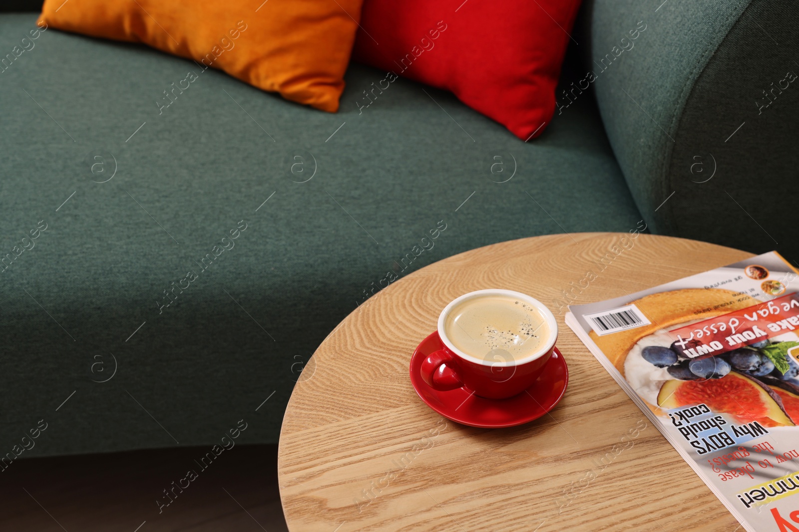 Photo of Wooden coffee table with cup of drink and magazine near sofa indoors, closeup