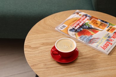 Photo of Wooden coffee table with cup of drink and magazine near sofa indoors, closeup