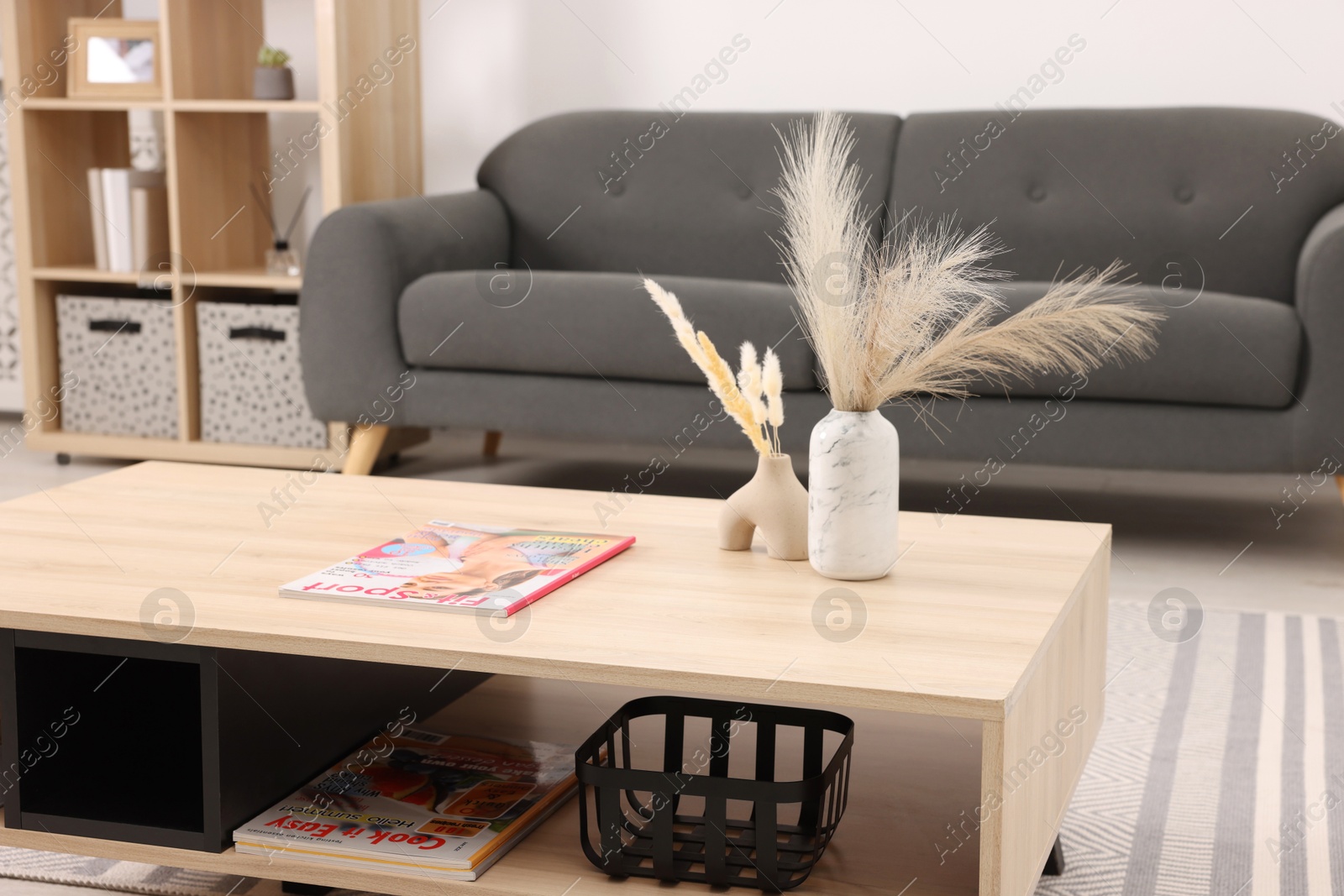 Photo of Stylish coffee table with decor and magazine near sofa at home, closeup. Interior design