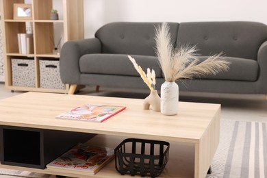 Photo of Stylish coffee table with decor and magazine near sofa at home, closeup. Interior design