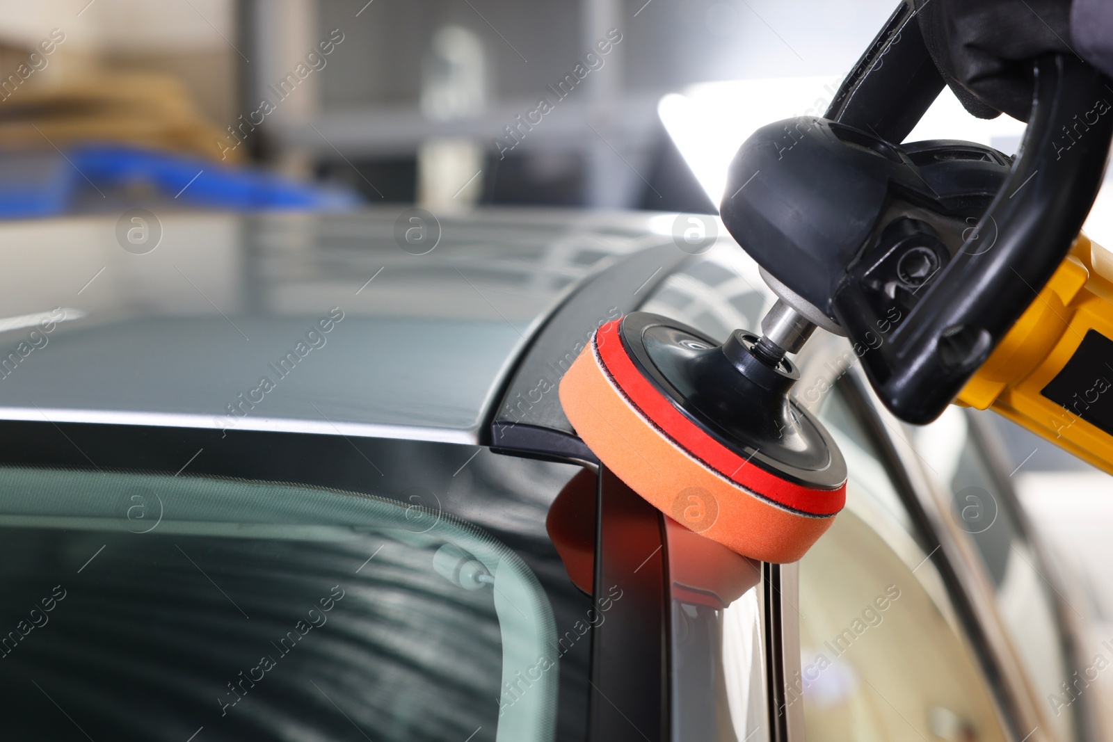 Photo of Man polishing car with orbital polisher indoors, closeup