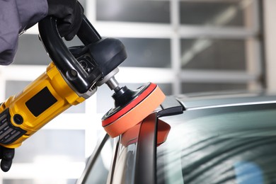 Photo of Man polishing car with orbital polisher indoors, closeup