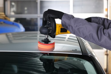 Photo of Man polishing car with orbital polisher indoors, closeup