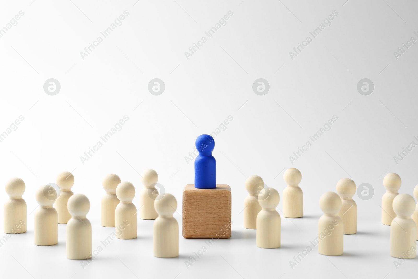 Photo of Human figures around wooden block with blue figure on top against white background. Competition concept