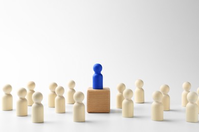 Photo of Human figures around wooden block with blue figure on top against white background. Competition concept