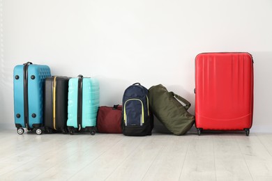 Photo of Colorful suitcases, backpack and bags on floor near white wall