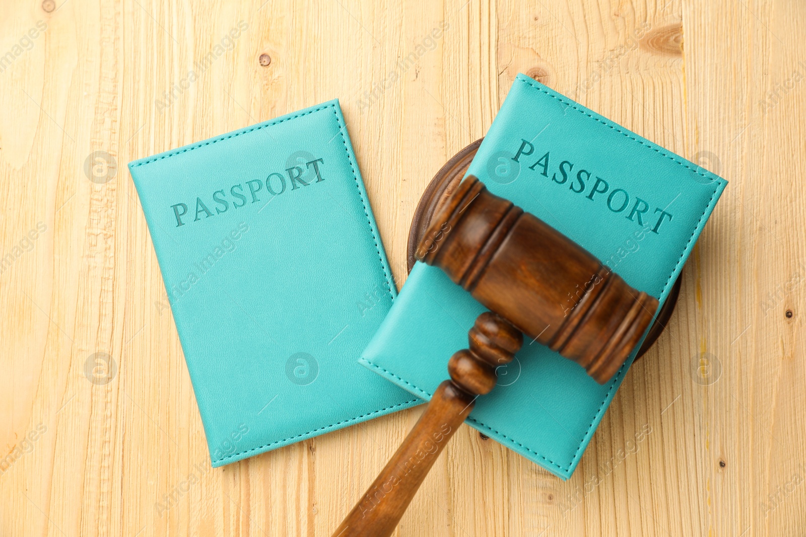 Photo of Passports in light blue covers and judge's gavel on wooden table, top view