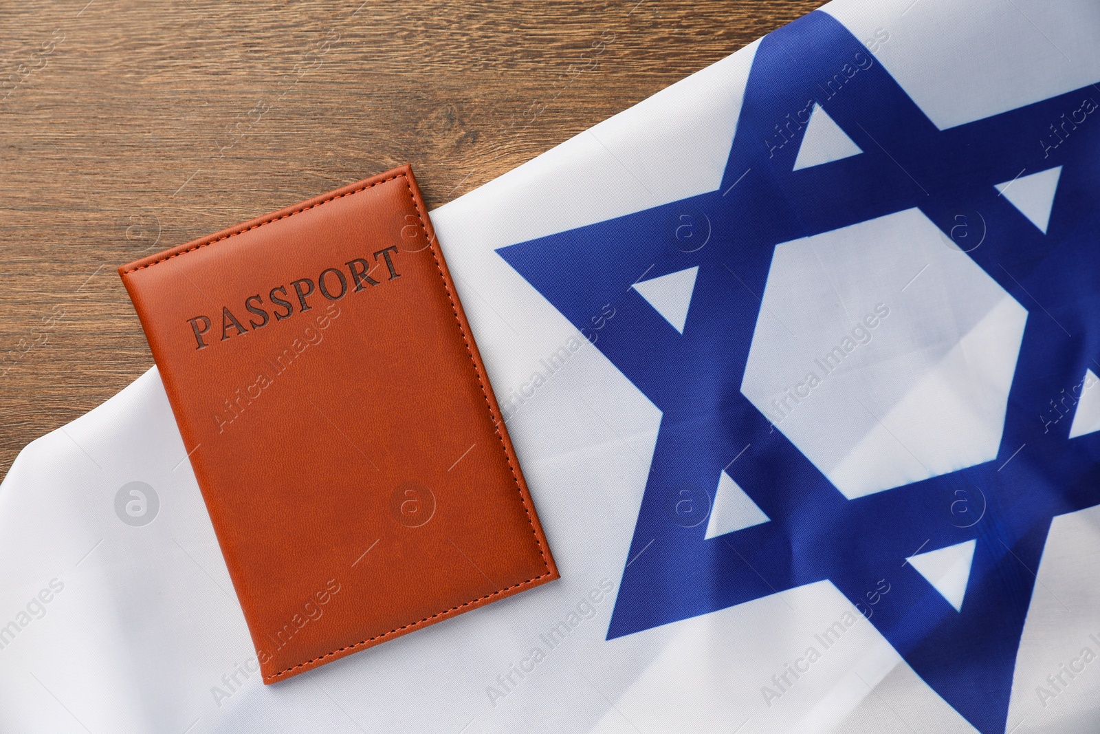 Photo of Passport in brown cover and flag of Israel on wooden table, top view