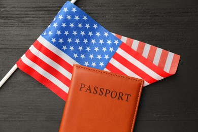 Photo of Passport in brown cover and flag of United States on black wooden table, top view