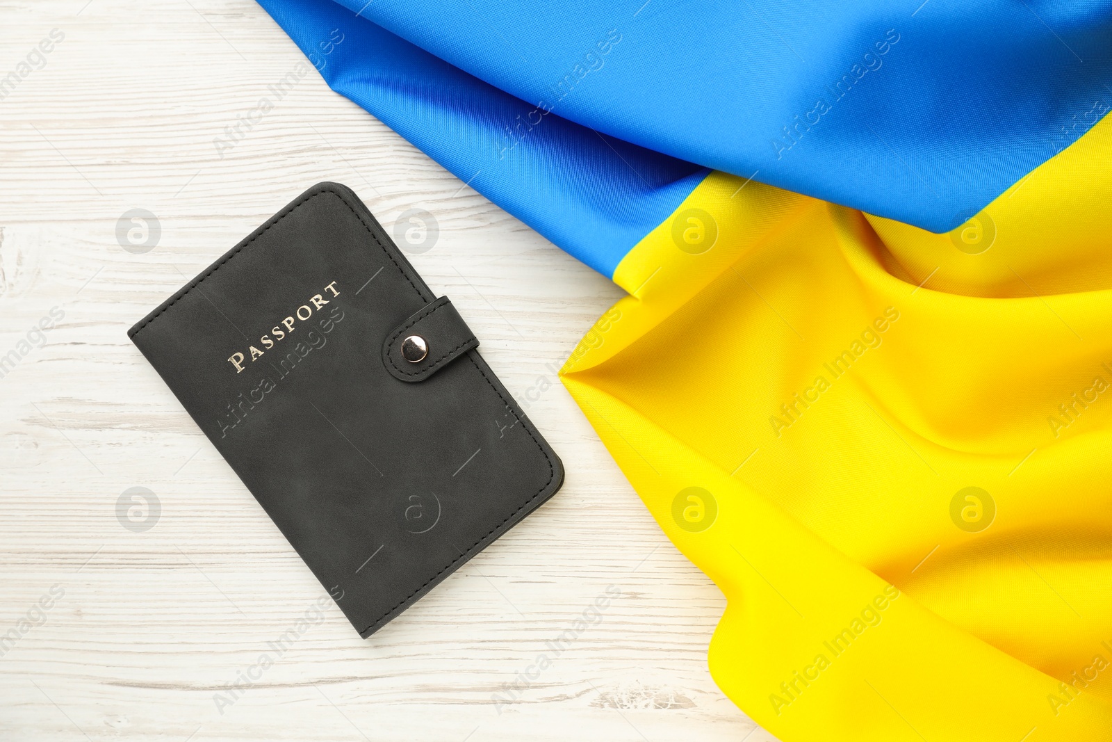 Photo of Passport in black cover and flag of Ukraine on light wooden table, top view