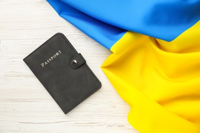 Photo of Passport in black cover and flag of Ukraine on light wooden table, top view