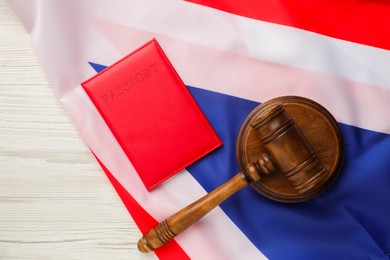 Photo of Passport in red cover, gavel and flag of United Kingdom on light wooden table, top view