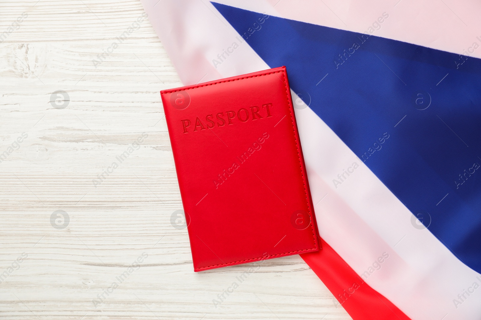 Photo of Passport in red cover and flag of United Kingdom on light wooden table, top view. Space for text