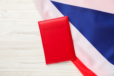 Photo of Passport in red cover and flag of United Kingdom on light wooden table, top view. Space for text