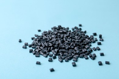 Pile of black plastic granules on light blue background, closeup