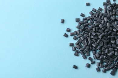 Photo of Pile of black plastic granules on light blue background, top view. Space for text