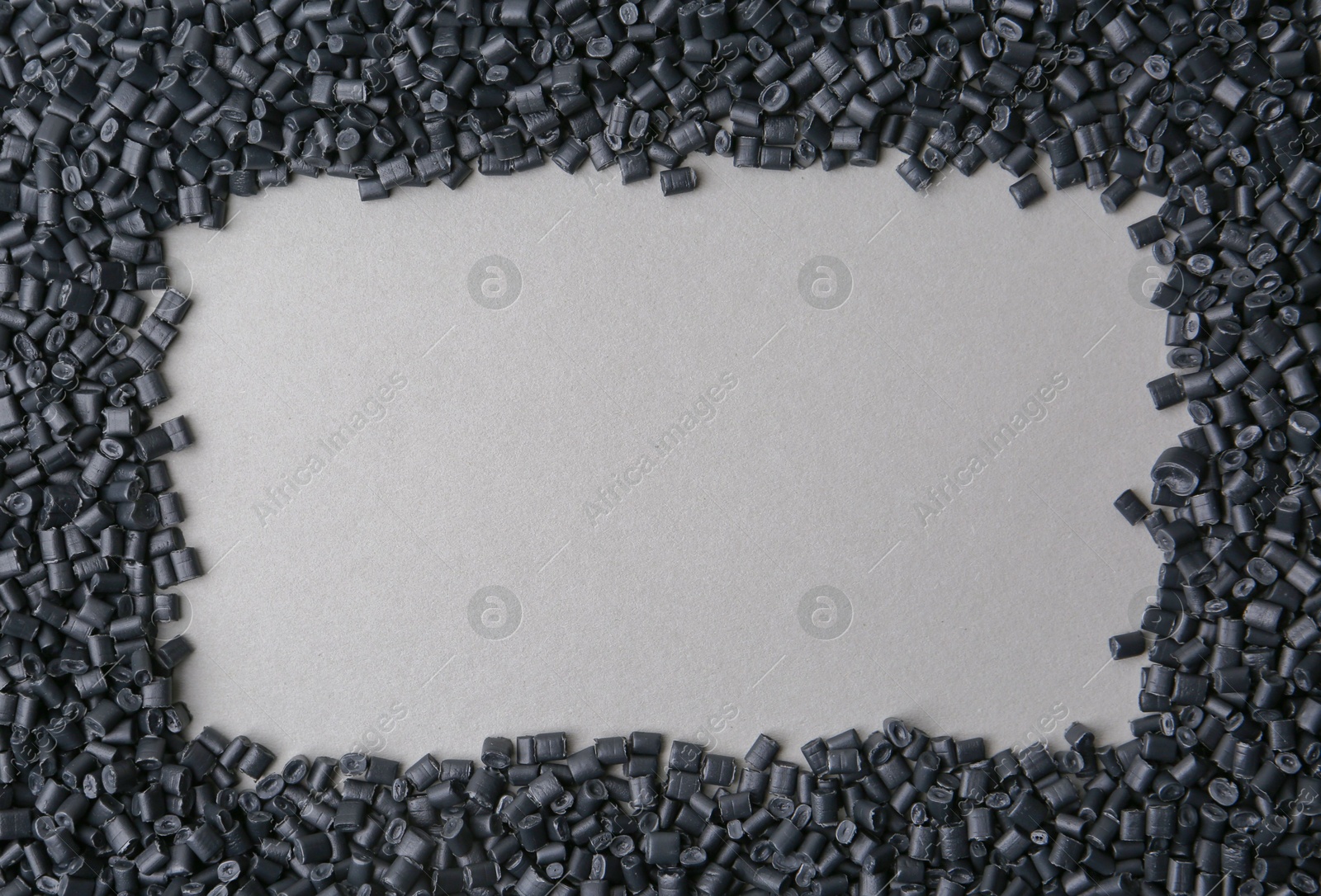 Photo of Frame of black plastic granules on grey background, top view. Space for text