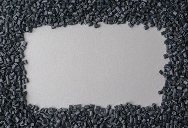 Frame of black plastic granules on grey background, top view. Space for text