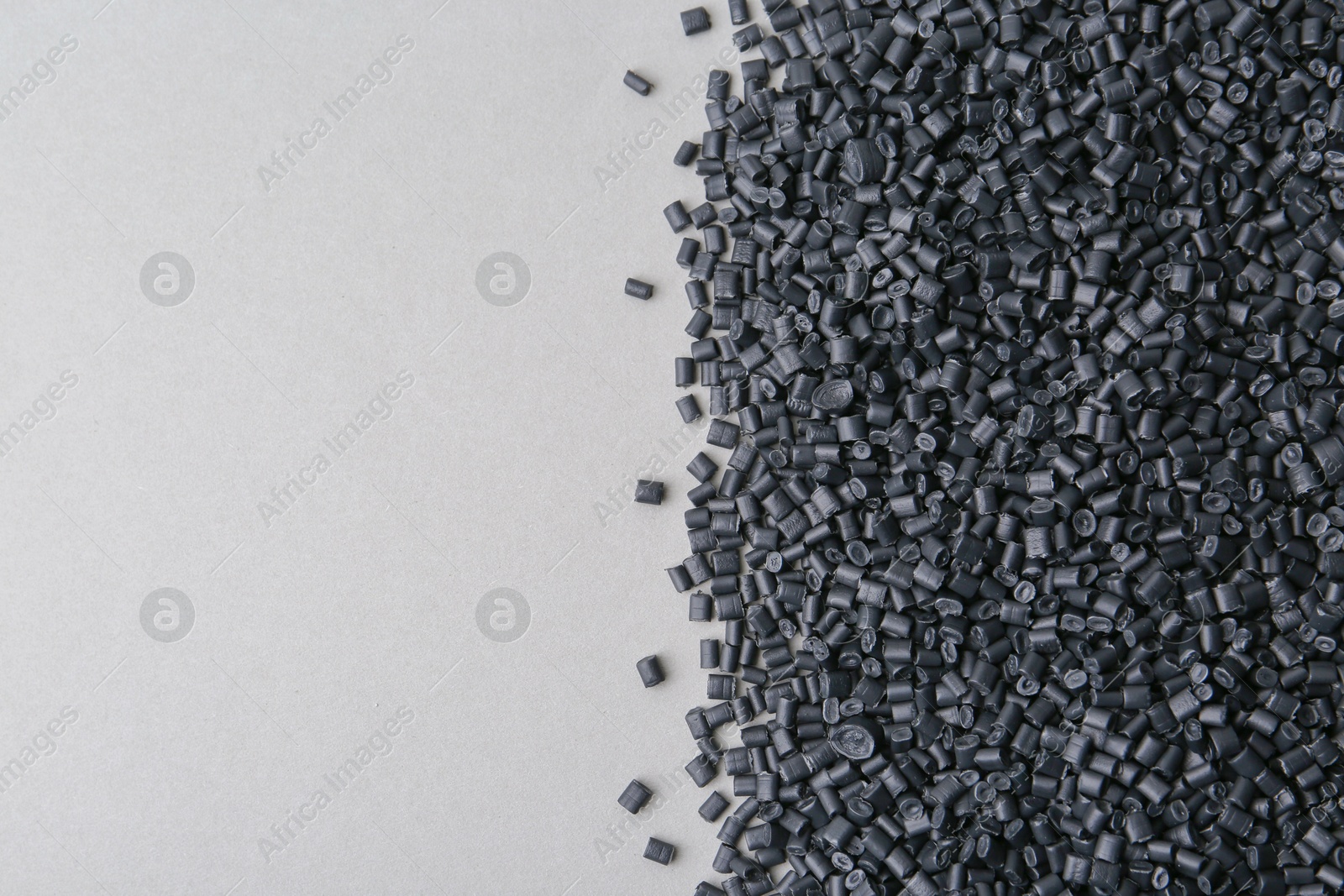 Photo of Pile of black plastic granules on grey background, top view. Space for text