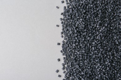 Pile of black plastic granules on grey background, top view. Space for text