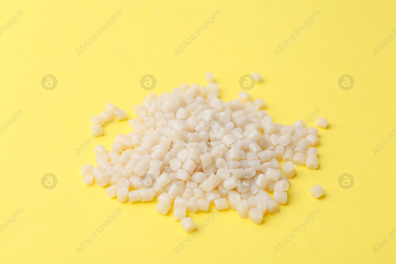 Photo of Pile of plastic granules on yellow background, closeup