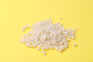 Photo of Pile of plastic granules on yellow background, closeup