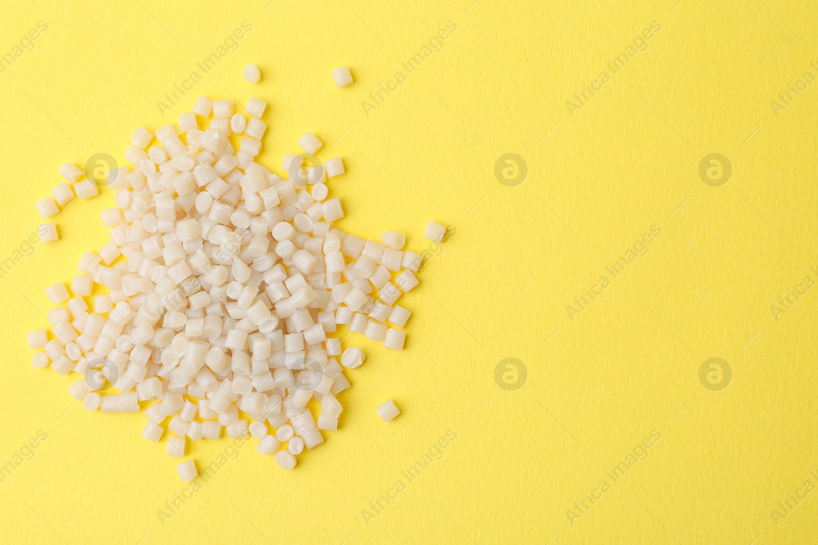 Photo of Pile of plastic granules on yellow background, top view. Space for text