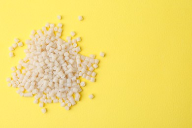 Photo of Pile of plastic granules on yellow background, top view. Space for text