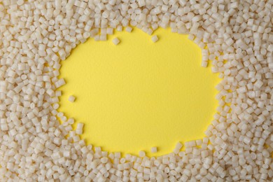 Frame of plastic granules on yellow background, top view. Space for text