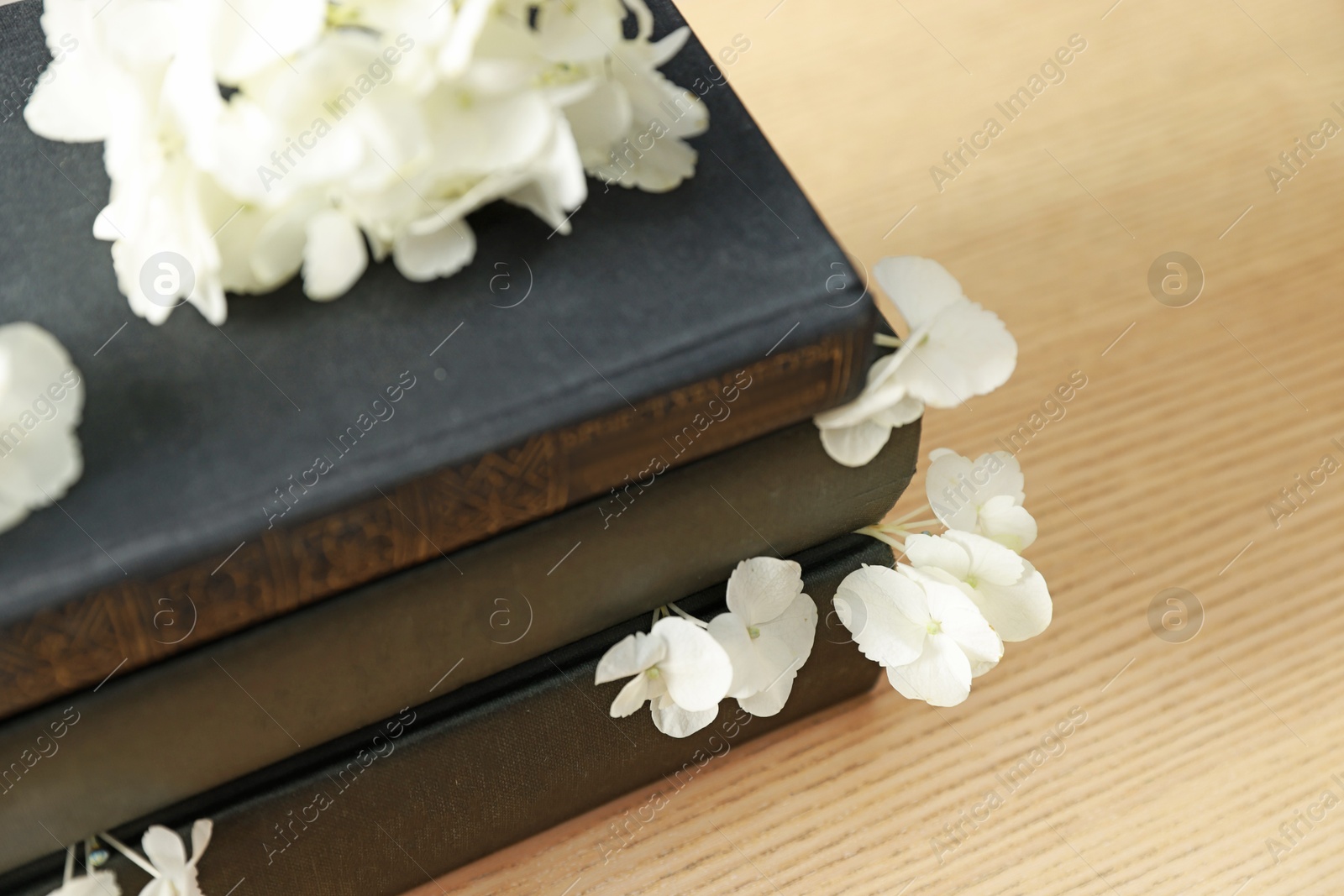 Photo of Stack of books and beautiful flowers on wooden table, closeup