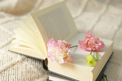 Photo of Open book with beautiful flowers on blanket, closeup