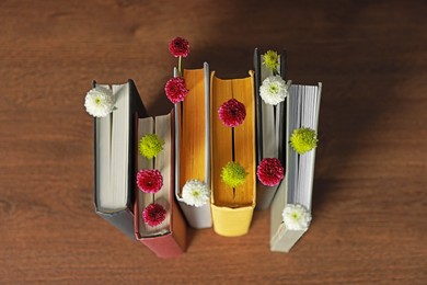 Photo of Different books with beautiful flowers on wooden table, above view