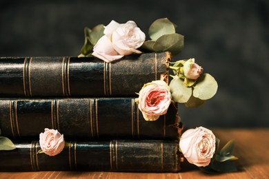 Photo of Stack of books with beautiful flowers and eucalyptus branches on wooden table, closeup