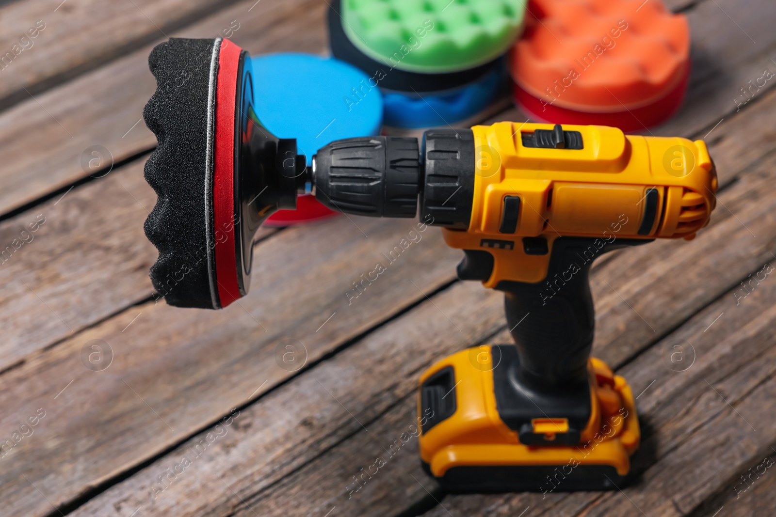 Photo of Electric screwdriver with different polish pads on wooden background, closeup