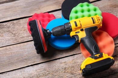 Photo of Electric screwdriver with different polish pads on wooden background, closeup