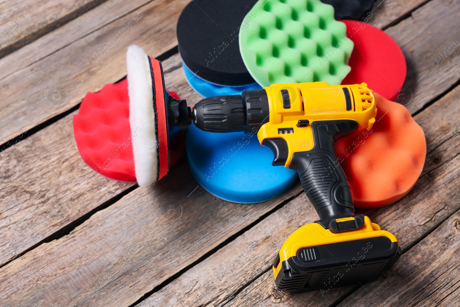 Photo of Electric screwdriver with different polish pads on wooden background