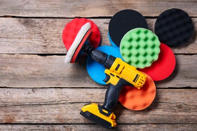 Photo of Electric screwdriver with different polish pads on wooden background, flat lay. Space for text